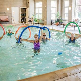 A group of older adults participating in a water aerobics class inside an indoor swimming pool.