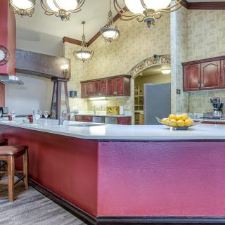 A spacious kitchen with red cabinetry, a large white countertop, and elegant chandeliers.