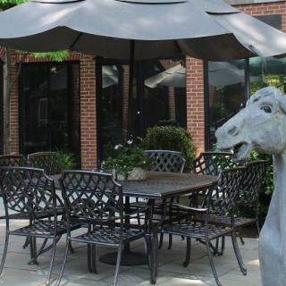 An outdoor patio setup with wrought iron furniture and a large umbrella, featuring a whimsical sculpture.