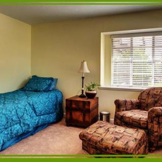 A cozy bedroom with a single bed, armchair, and ottoman next to a window.