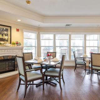 A cozy dining area featuring tables and chairs, with a fireplace and large windows providing ample natural light.