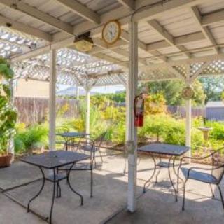 A shaded outdoor patio with metal tables and chairs, surrounded by a lush garden.