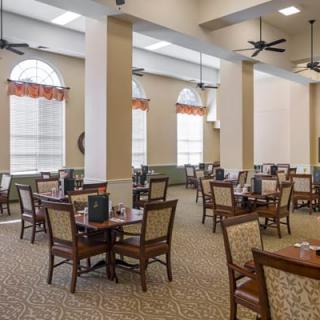 A spacious dining room with multiple tables and chairs, featuring large windows and overhead lighting.