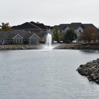 A view of suburban houses with a lake and fountain in the foreground.