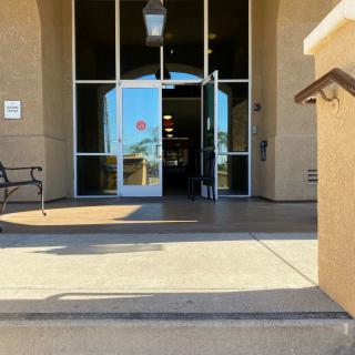 The entrance to a building featuring glass doors, with steps leading up and a bench to the side.