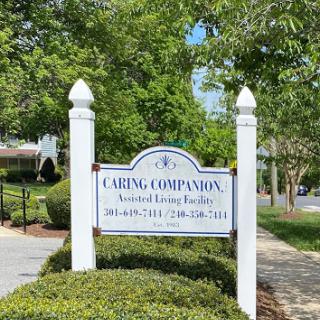 Sign for Caring Companion Assisted Living Facility, surrounded by lush greenery.