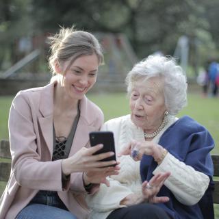 A young woman showing something on a smartphone to an elderly woman in a park.
