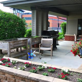 A cozy outdoor patio with gardening planters and seating area surrounded by flowers and greenery.