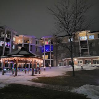 A winter night scene featuring a gazebo surrounded by snowy grounds and illuminated buildings.