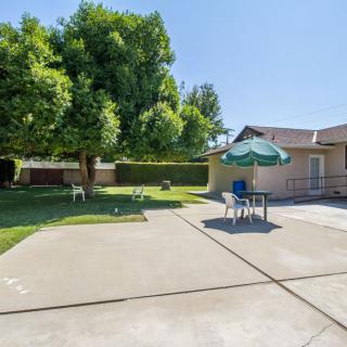 A sunny backyard with a patio featuring chairs and an umbrella, surrounded by grass and a large tree.