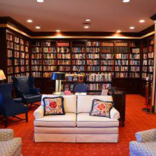 A cozy library room with shelves full of books, comfortable seating, and warm lighting.