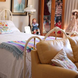 A cozy vintage-style bedroom with a bed, sofa, and decorative dolls.
