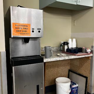 A water dispenser in an office kitchen area with a notice sign.