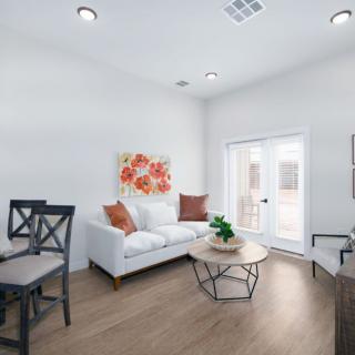 A bright and modern living room featuring a white sofa, colorful cushions, a round coffee table, and decorative wall art.