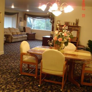 A cozy dining and living area with a table set, chairs, a sofa, and decor including flowers and a chandelier.