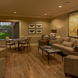 A cozy living room with comfortable seating and warm lighting, featuring artwork on the walls and a wooden floor.