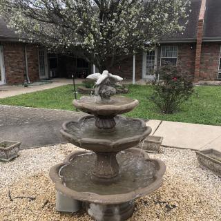 A three-tiered stone fountain in a courtyard surrounded by blooming trees and buildings.