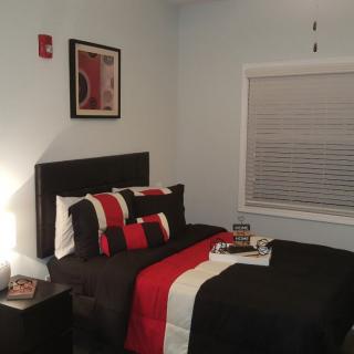A modern bedroom with a stylish black and red bedding set, featuring a framed artwork on the wall and a nightstand with a lamp.