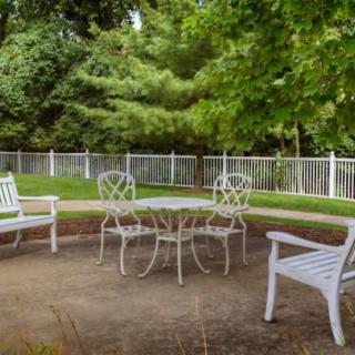 A peaceful outdoor patio area with white furniture surrounded by lush greenery.