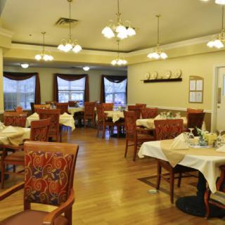 A cozy dining room with neatly arranged tables and chairs, featuring warm lighting.