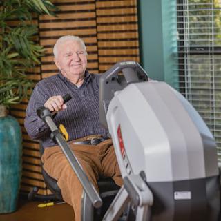 An elderly man engages in a workout using exercise equipment in a comfortable indoor environment.