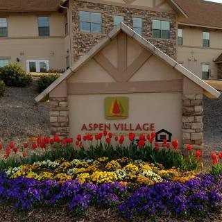 A well-maintained entrance of Aspen Village with vibrant flower beds and clear signage.