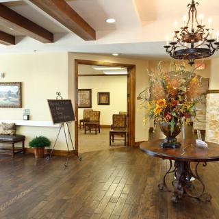 A warmly decorated lobby with wooden floors, a chandelier, and a floral centerpiece.