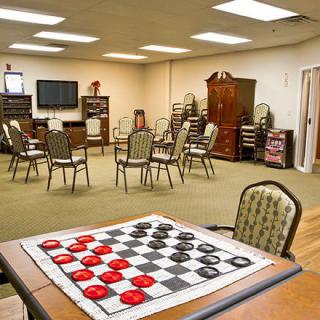 A recreation room with a checkers board in the foreground and seating arranged for group activities.