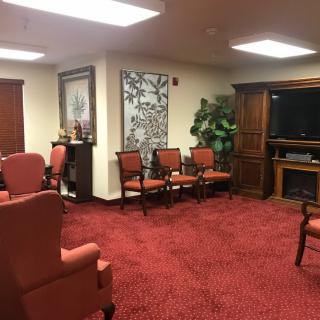 A waiting room with red carpeting, comfortable chairs, and a television.