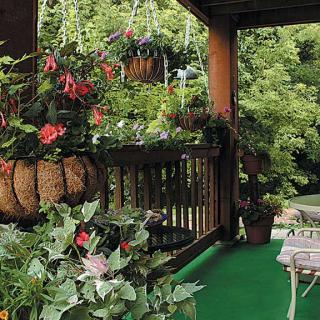 A cozy porch filled with vibrant flowers and lush greenery in hanging baskets.