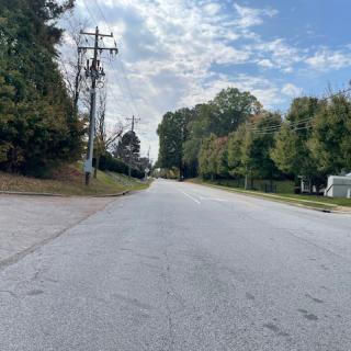 A quiet, tree-lined road under a partly cloudy sky.