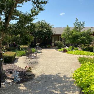 A beautiful garden with a paved pathway and seating surrounded by lush greenery under a clear blue sky.