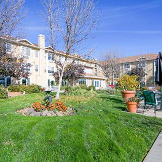 A well-maintained garden area in front of an apartment building with lush green grass, trees, and potted plants.