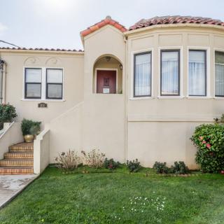 A Spanish-style stucco house with a manicured lawn and arched entryway.