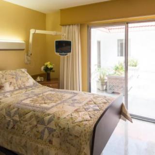 A hospital room with a bed, TV, and window leading to an outdoor area.