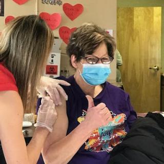 A cheerful patient gives a thumbs up after receiving a vaccination in a clinic.