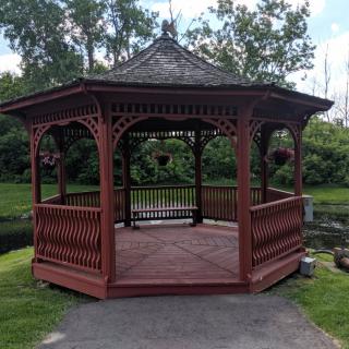 A wooden gazebo in a park surrounded by greenery.