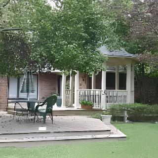 A cozy garden view with a house, deck, and gazebo surrounded by trees.
