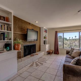A cozy living room featuring a television, bookshelves, and natural light from a large window.