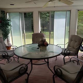 A cozy patio seating area with a glass table and cushioned chairs, surrounded by sliding glass doors and an indoor plant.