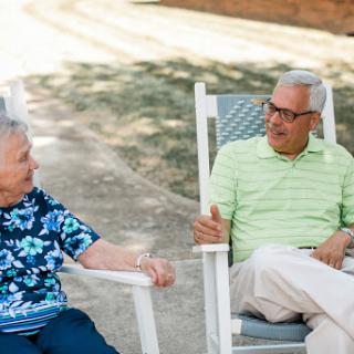 Two seniors enjoying a friendly conversation in rocking chairs outdoors.