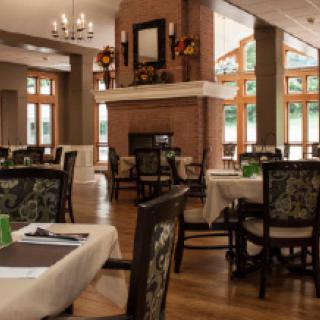 A cozy dining area with elegantly set tables and chairs, a central fireplace, and a chandelier overhead.