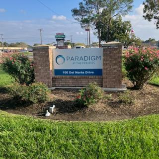 An exterior view of a business sign surrounded by greenery and a clear blue sky.
