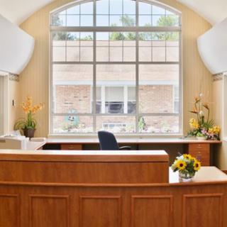 A reception area with a wooden desk, flowers, and a large window.