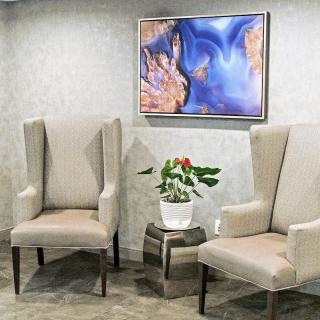 Elegant waiting area with two beige chairs, a small table with a plant, and abstract artwork on the wall.