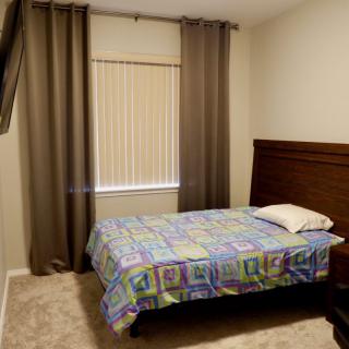 A neatly arranged bedroom with a single bed, curtains, and window blinds.
