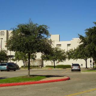 A building surrounded by trees and a parking lot with cars on a sunny day.