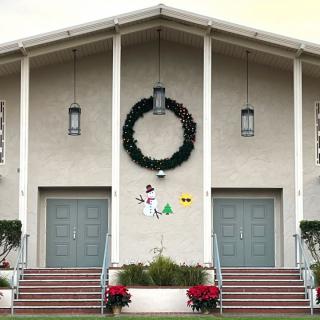 A church building decorated with a large wreath and poinsettias for the holidays.