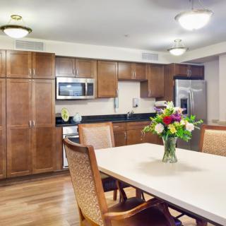 A modern kitchen and dining area featuring wood cabinets, stainless steel appliances, and a table with flowers.