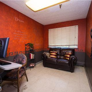 A cozy office space with red walls, featuring a desk with a computer and a comfortable sofa.